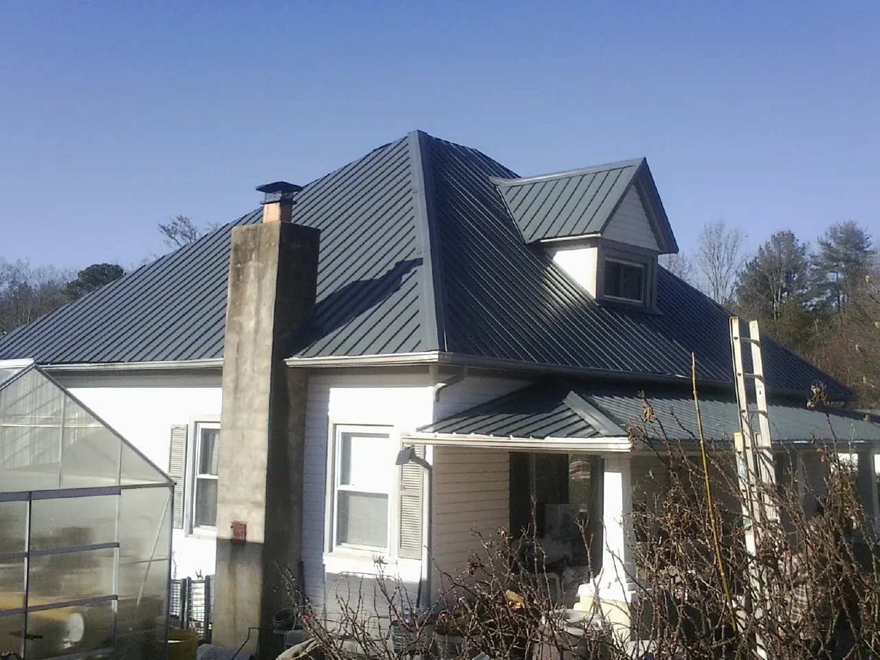 Dark blue standing seam metal roof on a white farmhouse with dormer — Slate & Tile Roof Repair by Roofing Brothers in Clarkesville