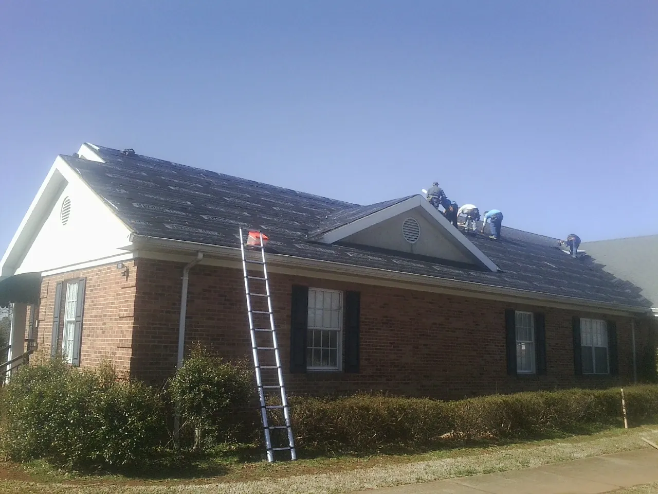 Crew tearing shingles off a brick ranch roof with a ladder set — Emergency Roof Repair work by our crew in Clarkesville