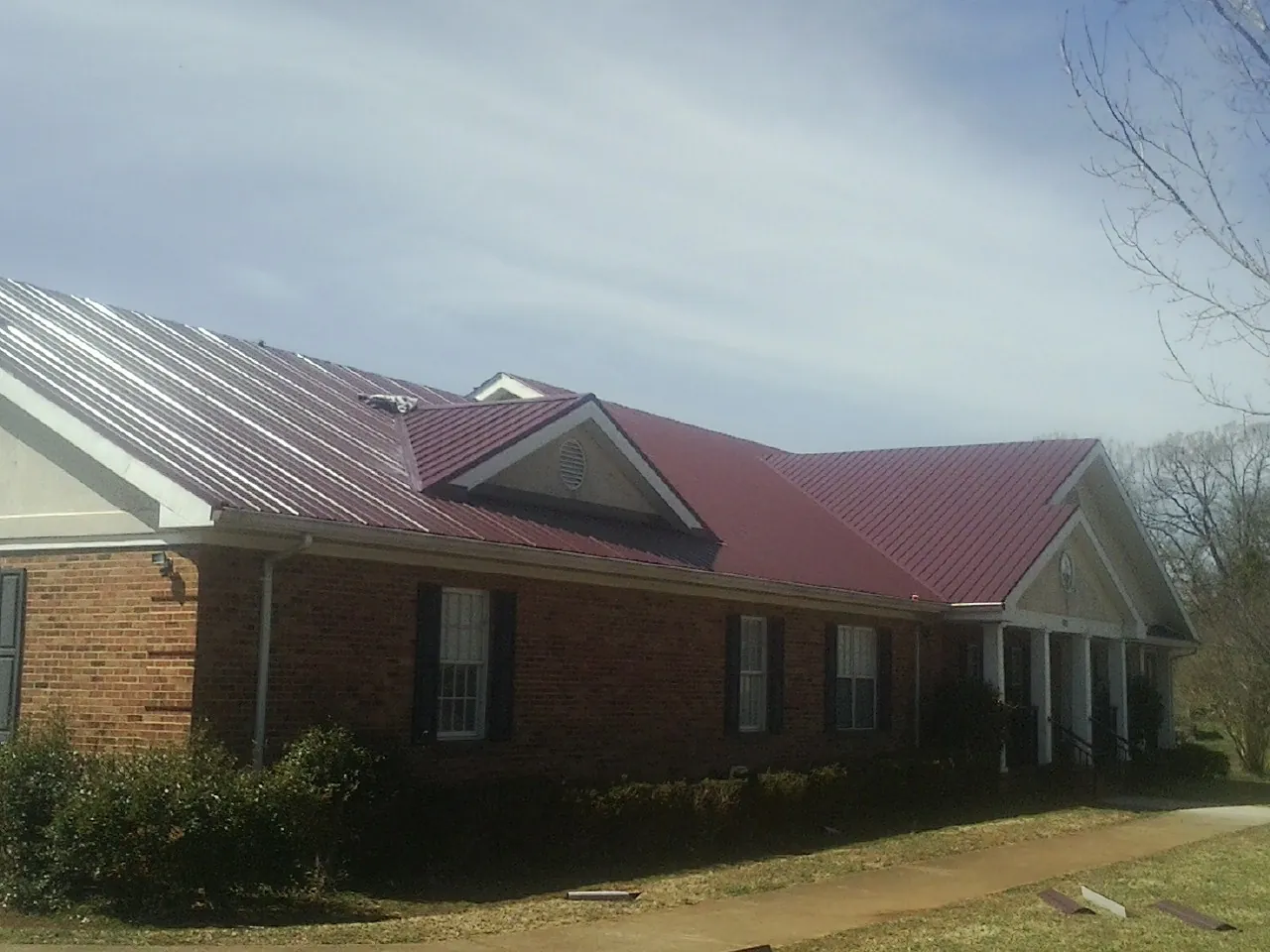 Red metal roof with gabled entries on a long brick building, from a Hail Damage Roof Repair job in Clarkesville