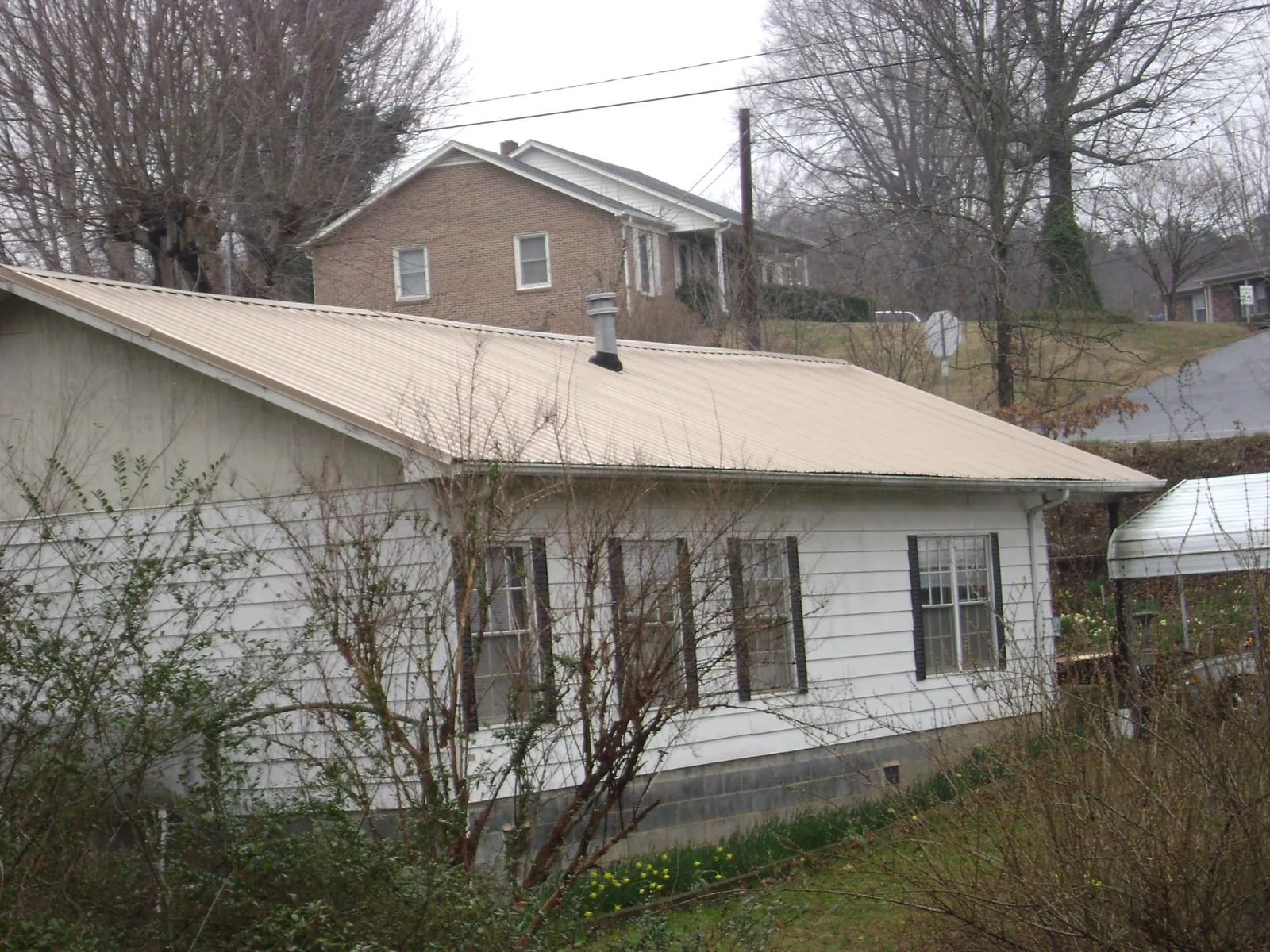 Tan metal roof on a white sided house set into a hillside — Commercial Roofing by Roofing Brothers in Clarkesville