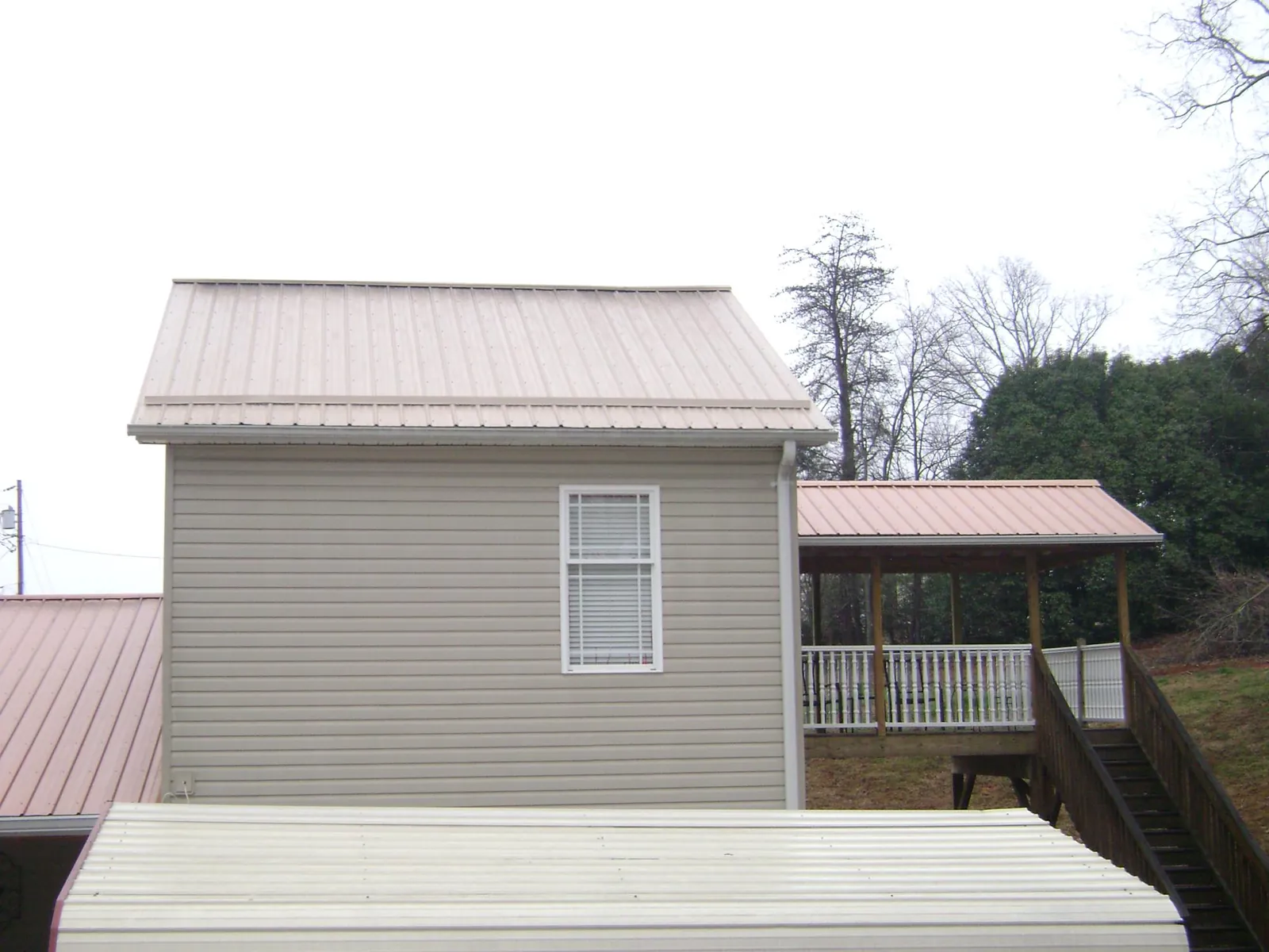 Tan metal roofs on a two story addition and attached porch, from a Roof Replacement job in Clarkesville